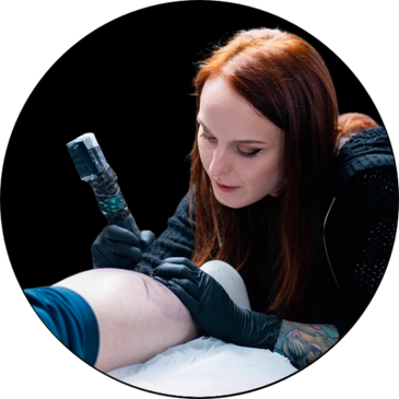 Woman tattoo artist working on a client's leg.