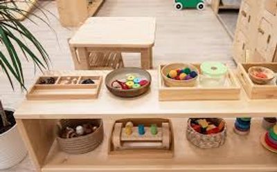 Low wood shelf with Montessori works neatly arranged trays and baskets. 