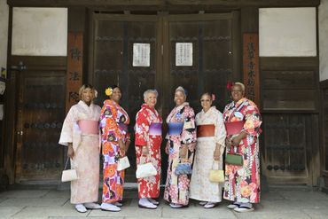 Group of women in colorful traditional kimonos standing in front of a wooden door.