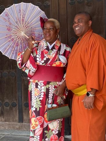 A couple dressed in traditional Japanese attire, smiling and posing with a parasol.