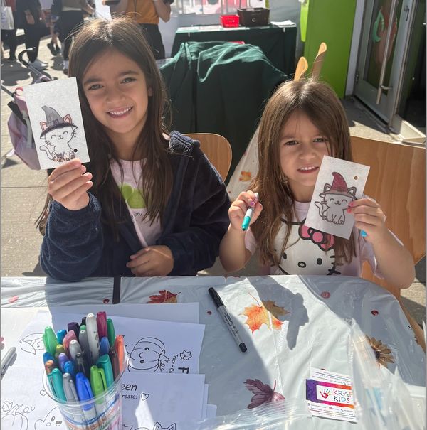 Two girls proudly show their Halloween-themed cat drawings.