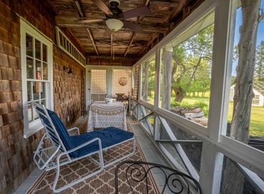 Cozy screened porch with a cushioned lounge chair and a dining table overlooking a green yard.