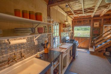Rustic kitchen with open shelves, vintage stove, and wooden accents overlooking a scenic field.