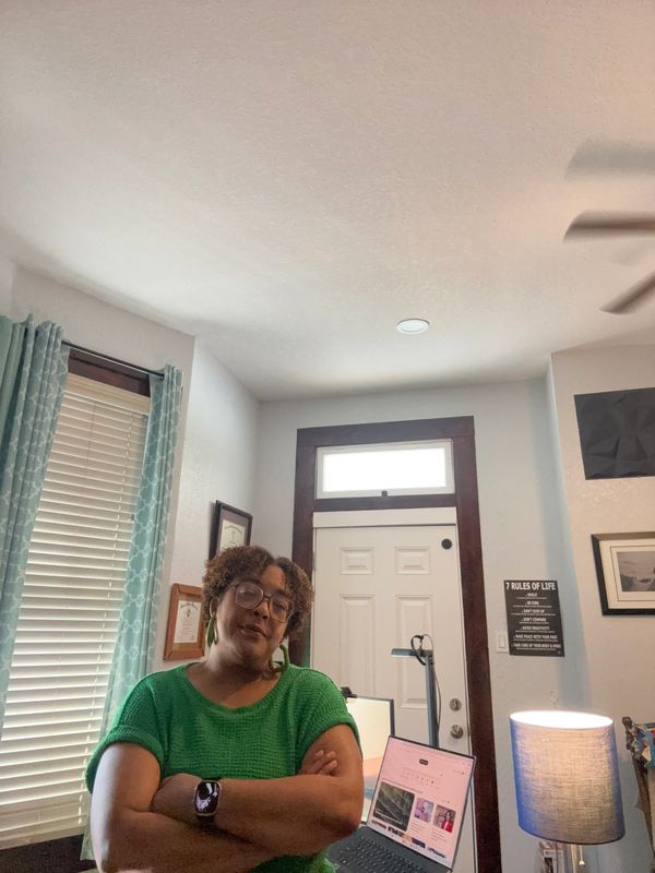 Woman in green shirt standing confidently in a cozy home office.