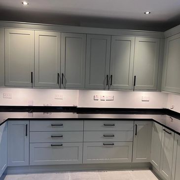 Modern kitchen with gray cabinets and black countertops under recessed lighting.