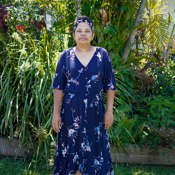 Woman in a floral navy dress standing in a garden with greenery.