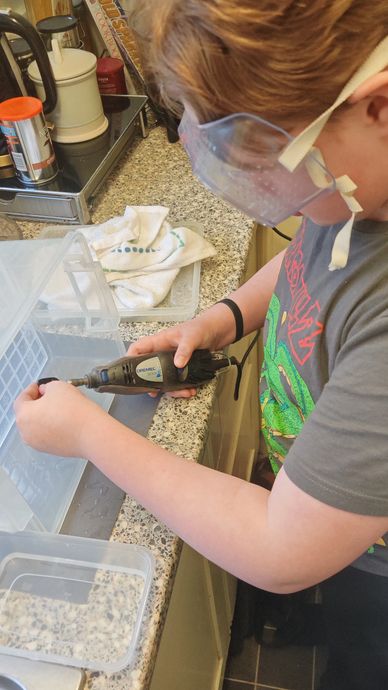 Boy using a Dremel multi hand tool to grind the back of fused glass wearing goggles