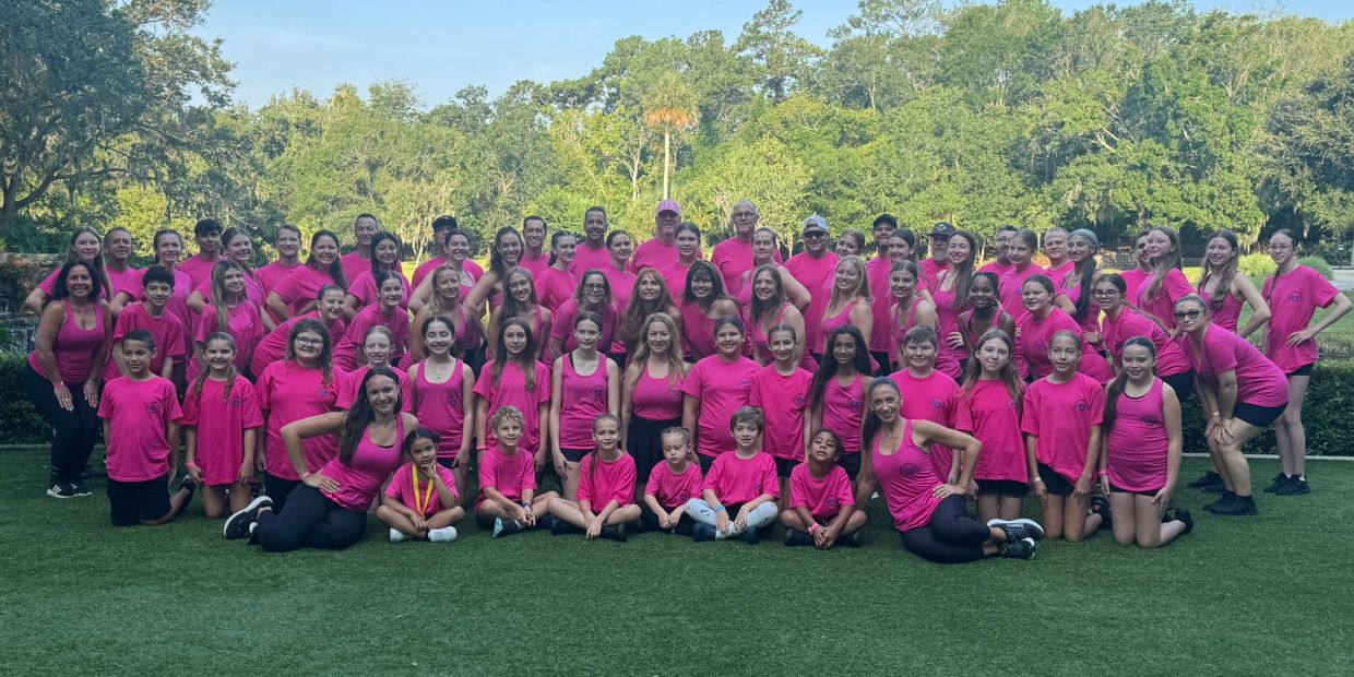 Large group of people wearing pink shirts outdoors on grass.