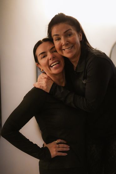 Two women smiling and hugging warmly indoors.