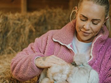 Woman in pink jacket gently petting a fluffy bunny indoors.