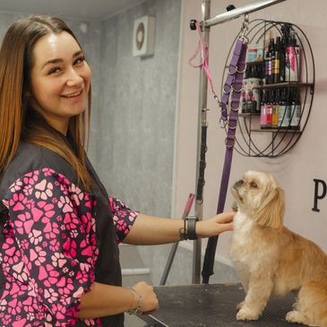 A smiling groomer with a small dog on a grooming table.