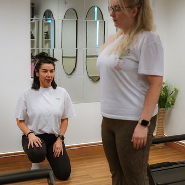 A fitness instructor guides a woman during a workout session indoors.