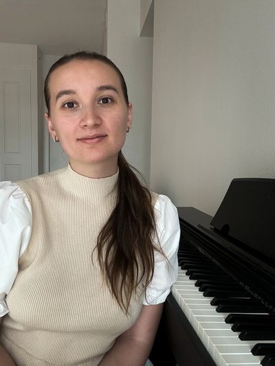 A young woman sits beside a piano, smiling gently at the camera.