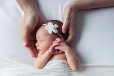 Newborn photoshoot; parent hands on baby in white 