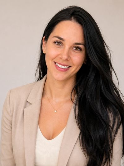 Femme souriante aux cheveux longs et noirs, vêtue d'un blazer beige.