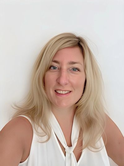 Smiling woman with blonde hair in a white top against a plain background.