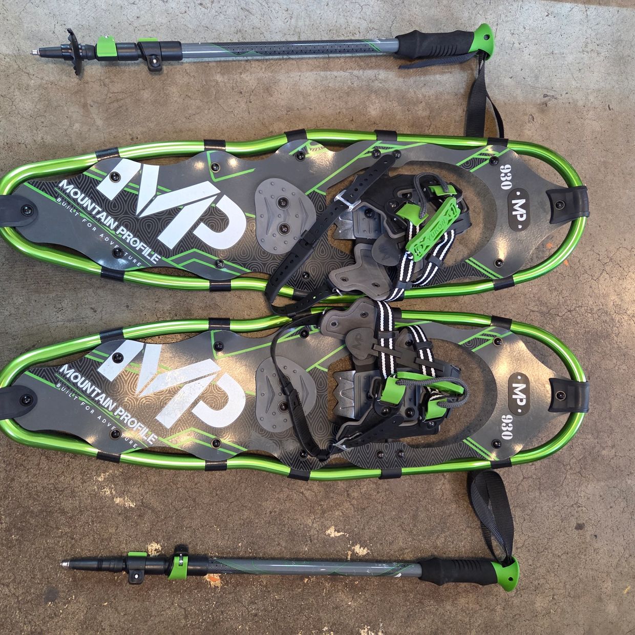 Pair of green snowshoes and two trekking poles on concrete.