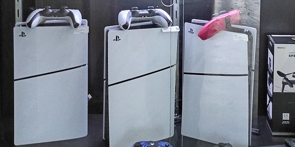 Three white PlayStation consoles with controllers on top.