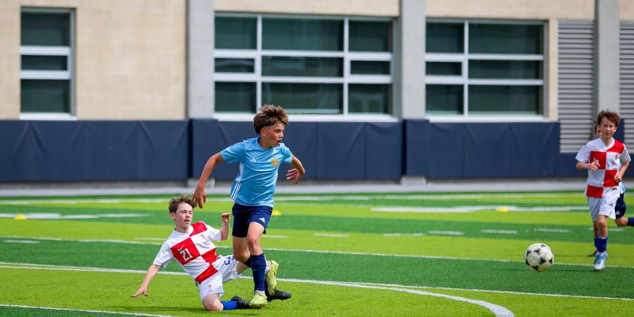 Boys playing soccer on a green turf field.