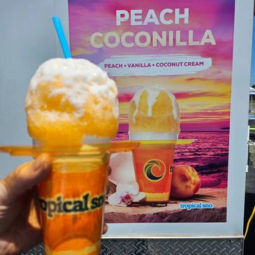 Hand holding a peach-flavored shaved ice in front of a colorful Tropical Sno advertisement.