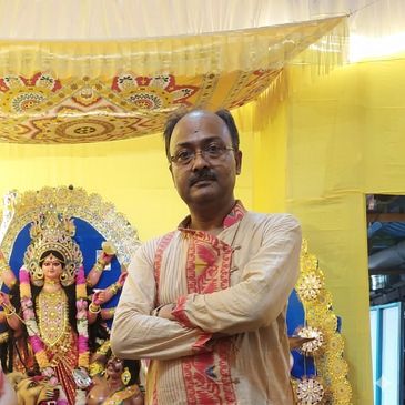 Man standing with arms crossed near a decorated Durga idol.