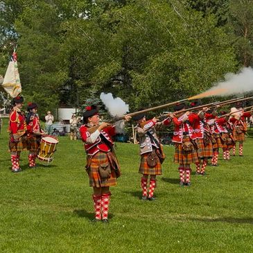 Scottish soldiers in traditional attire firing muskets during a ceremonial event.