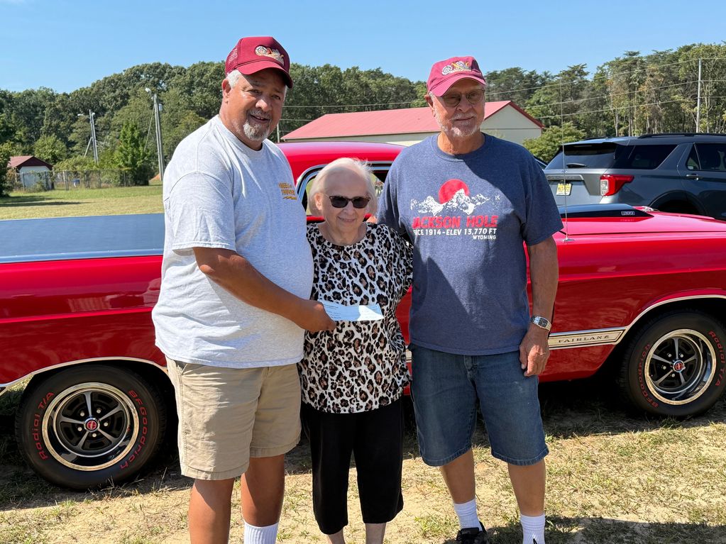 Three people standing in front of a red car on a sunny day.