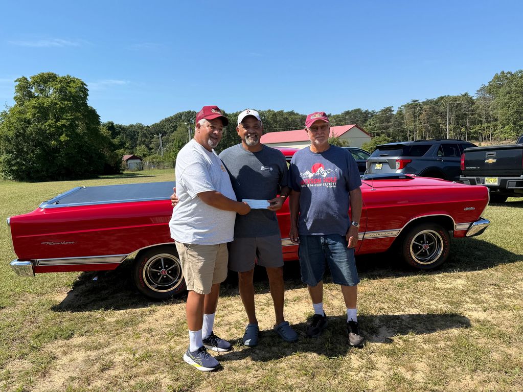 Three men standing in front of a red classic car outdoors.