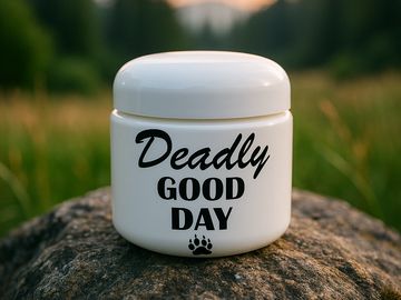 White jar with 'Deadly Good Day' text on rock outdoors.