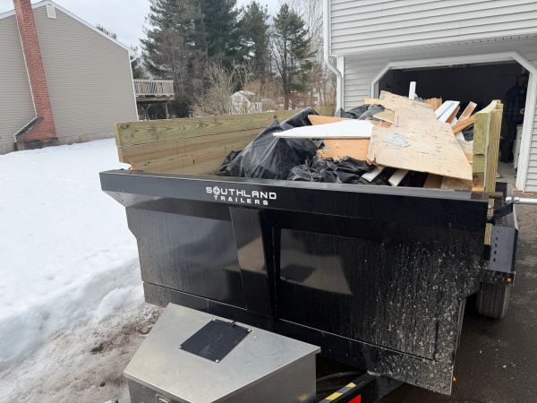 Black Southland trailer filled with wood debris near a snowy driveway.