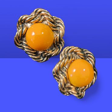 Vintage gold-tone earrings with bright orange centers on a blue background.