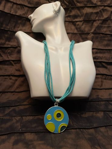 Turquoise necklace with a circular pendant featuring yellow and blue abstract patterns.