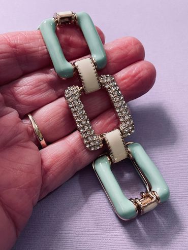 Hand holding a decorative bracelet with pastel and rhinestone links.