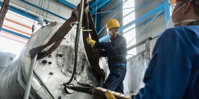 Workers in safety gear handling large industrial equipment inside a factory.