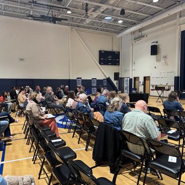 Audience seated in gymnasium listening to speaker.