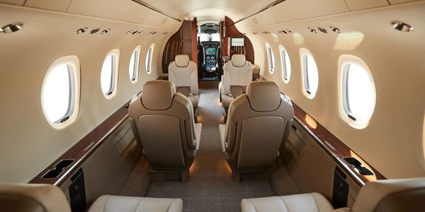 Luxurious interior of a private jet with beige leather seats and oval windows.