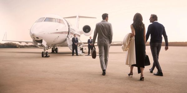 Three stylishly dressed people walking towards a private jet on the runway.