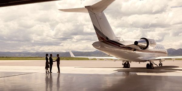 Business people shaking hands near a private jet in a hangar.
