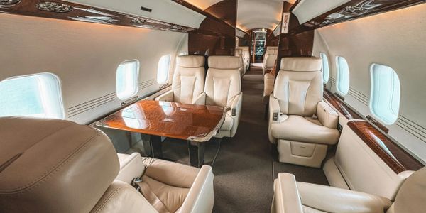 Luxurious private jet interior with beige leather seats and wood-finished table.