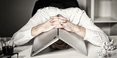 Exhausted Man. Burnout from work. The sitting at the desk, his head is underneath his opened laptop.