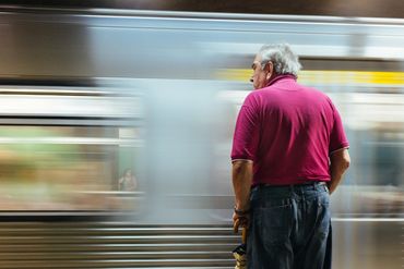 An elderly man in a red shirt waits as a train speeds past.