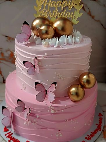 Elegant two-tier pink birthday cake with golden spheres and delicate butterfly decorations.
