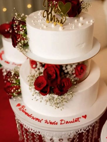 Elegant white wedding cake adorned with red roses and delicate baby's breath flowers.