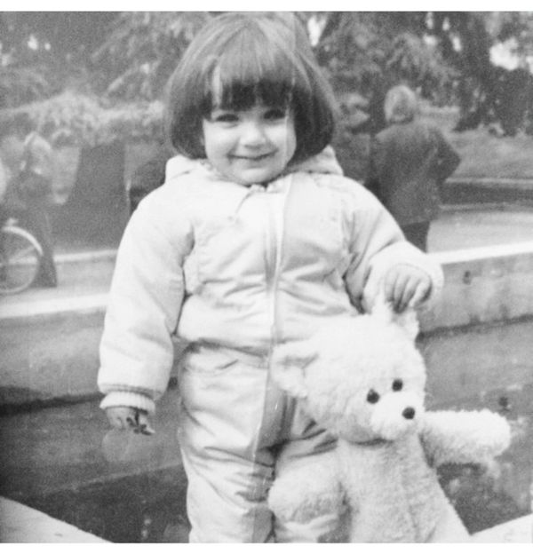 A smiling child in winter clothes holding a teddy bear outdoors.