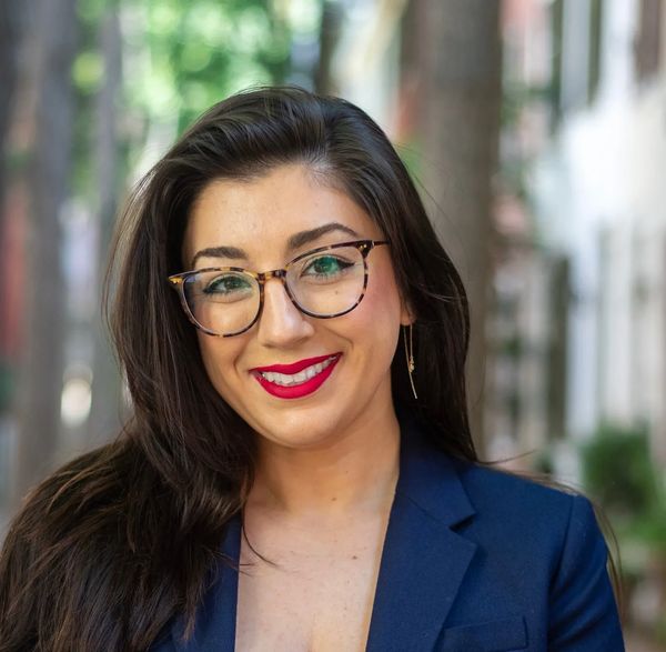 Confident woman with glasses and red lipstick smiles outdoors.