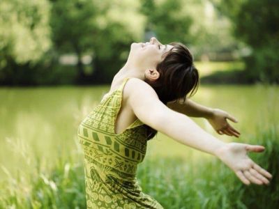 Woman in green dress enjoying nature with arms outstretched.