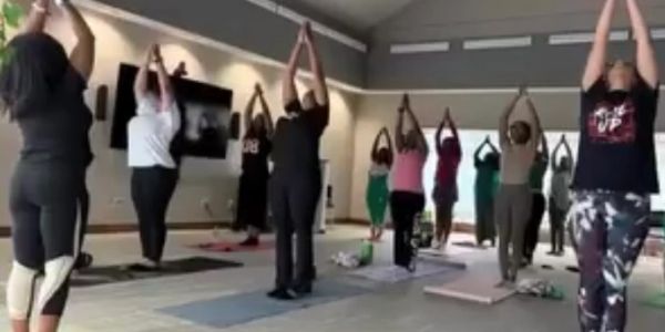 Group practicing yoga indoors with arms raised in tree pose.