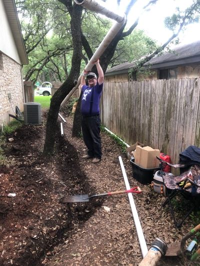 A plumber holds up a long section of sewer pipe he's about to place into a side-yard trench