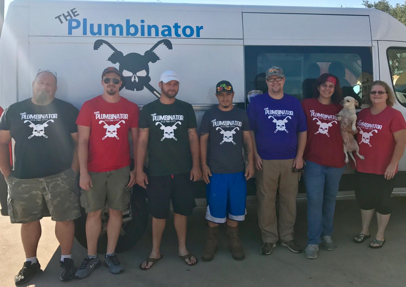 Group of plumbers standing next to a work van. The Plumbinator logo is a skull and cross wrenches.