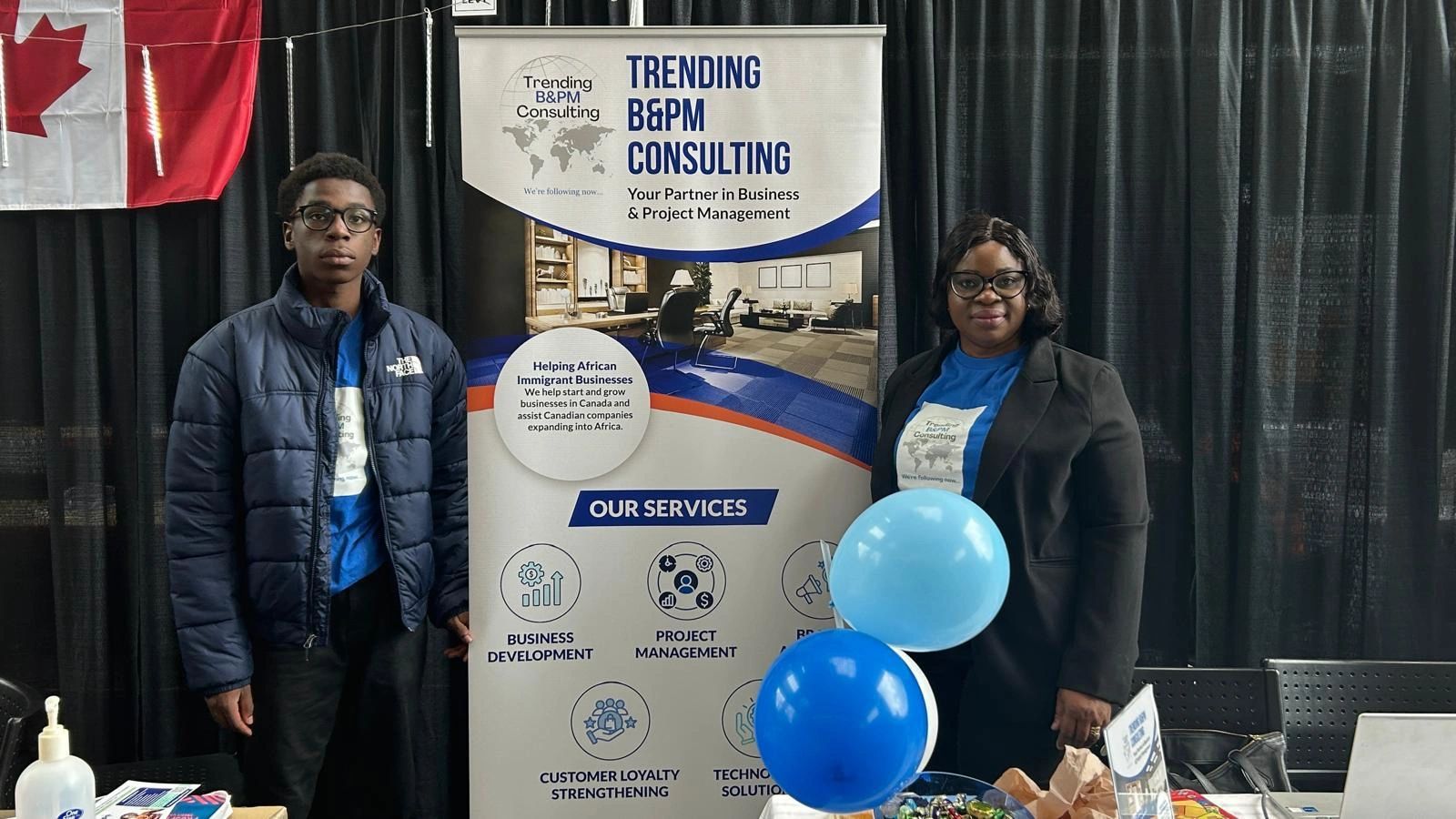 Two individuals stand by a consulting services banner with Canadian flag in background.
